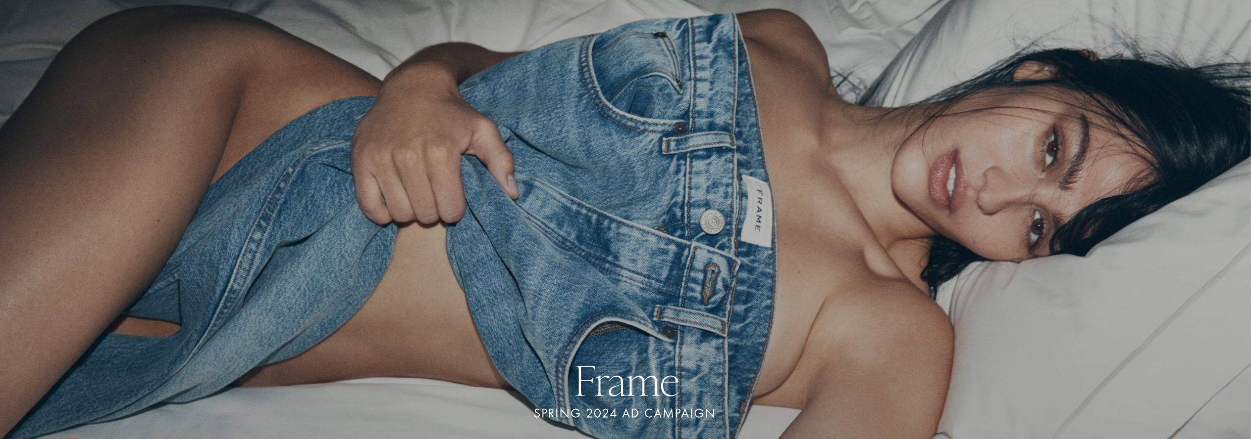 In a Frame clothing ad, a woman lies naked on a bed with a pair of jeans draped over her form.